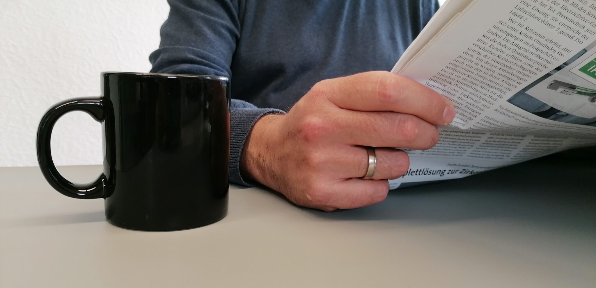 Person liest eine Mitarbeiterzeitung, die Platz für komplexe Themen in Wort und Bild bietet, im Vordergrund steht eine Kaffeetasse.