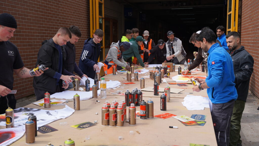 Kreativaktion mit Partnermarken beim United by Tools Event Auszubildende gestalten eigene T-Shirts mit Sprühdosen und Motiven der Partnermarken